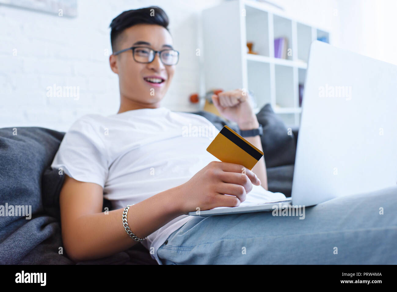 Stattliche asiatischer Mann mit Laptop auf dem Sofa und die Kreditkarte zu begeistern Stockfoto