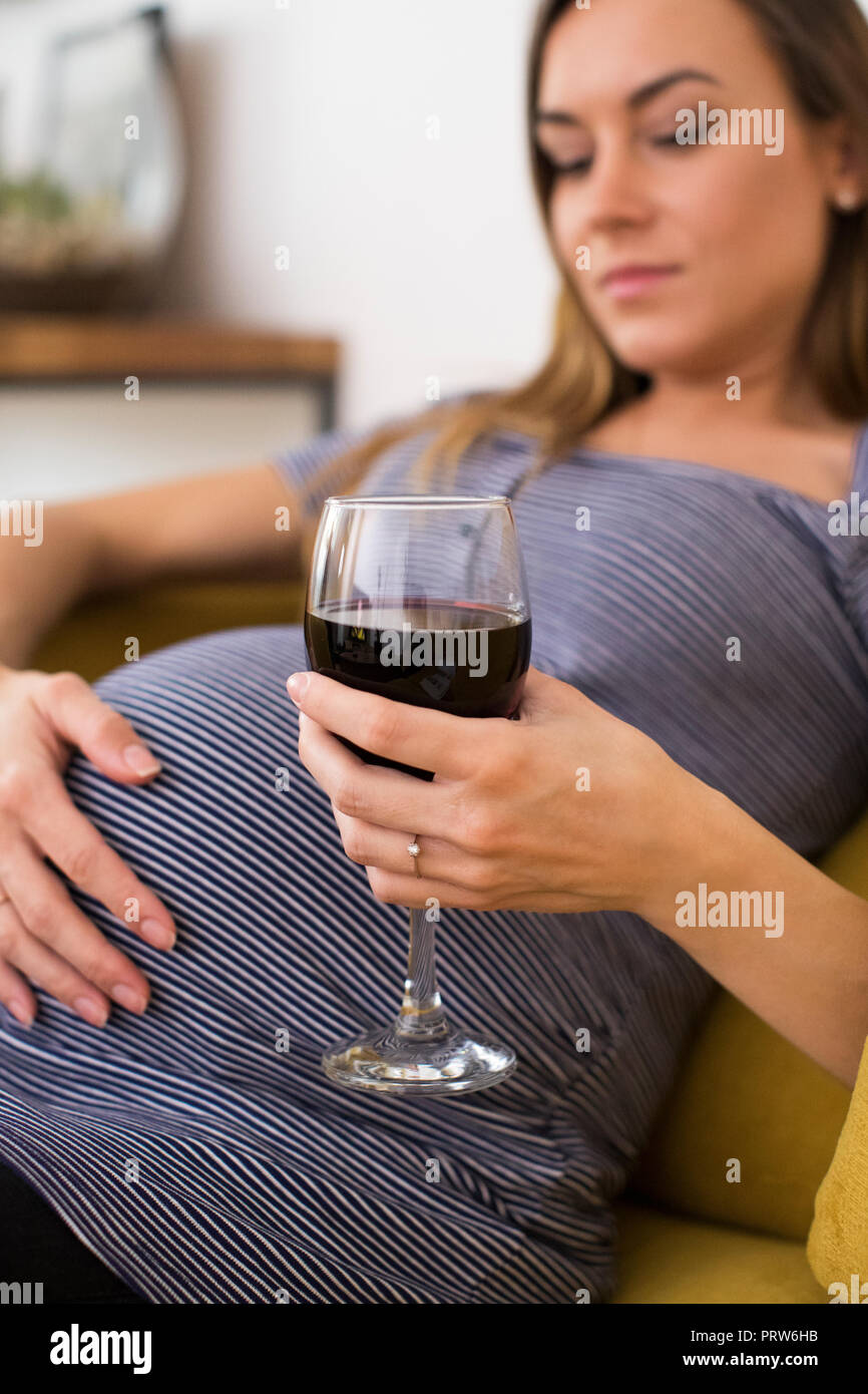 Betroffene schwangere Frau trinkt Rotwein zu Hause Stockfoto