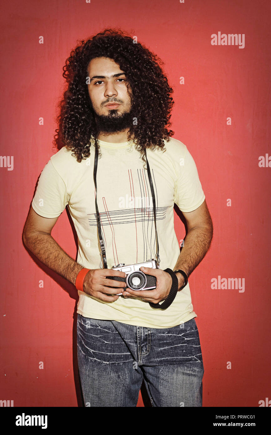 Nahaufnahme von einem stattlichen leidenschaftlich expressive cool Junge brünette Fotografin Männer mit langen Locken mit einem Vintage Spiegelreflexkamera stehend gegen Stockfoto