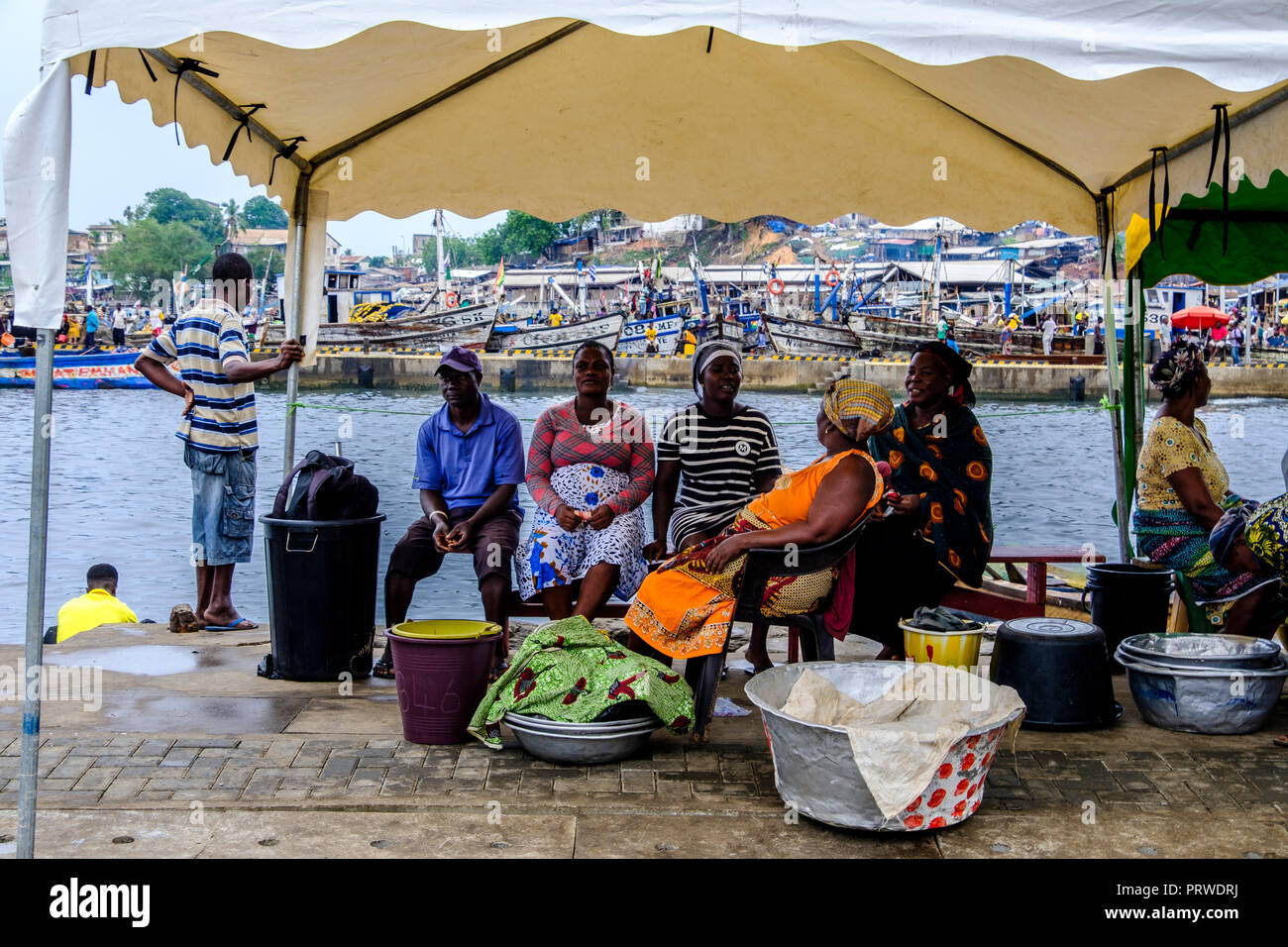 SEKONDI TAKORADI, GHANA - 10. APRIL 2018: Frauen in bunten Kleid warten mit ihrer Dose Eimer für Fische an belebten Bosomtwi Sam Angeln Harbou angelandet werden. Stockfoto