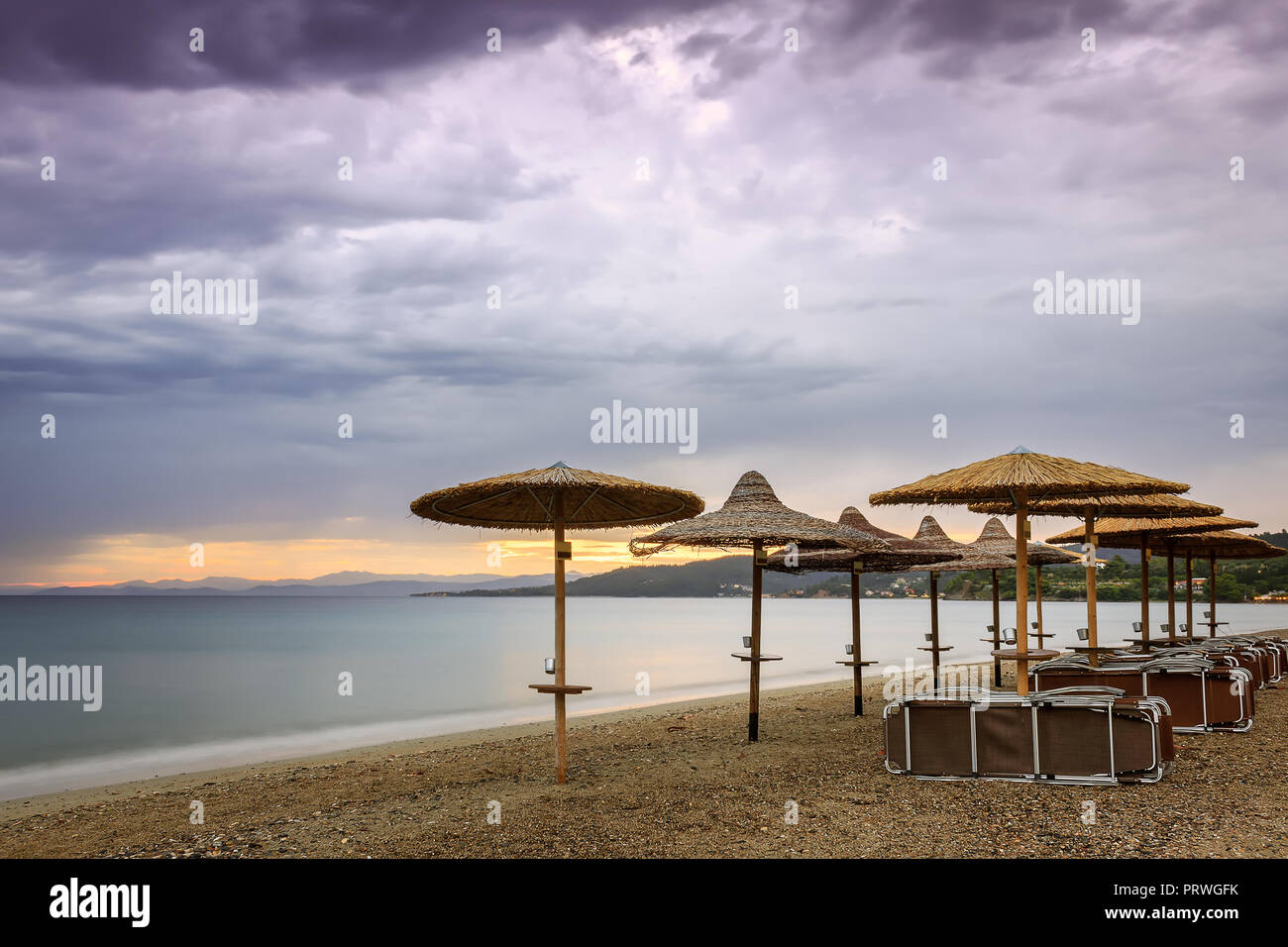 Stroh Strand Sonnenschirm, Liegestühle, Sonnenuntergang Himmel und seidig, Meer Wasser in Griechenland Stockfoto