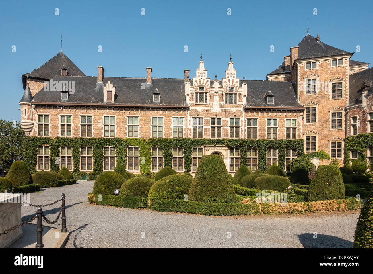 Gaasbeek, Flandern, Belgien - 14. September 2018: Südwesten Flügel des Schloss Gaasbeek mit grünem Garten vor, hellbraunen Wänden, dunklen Dach unter Blu Stockfoto