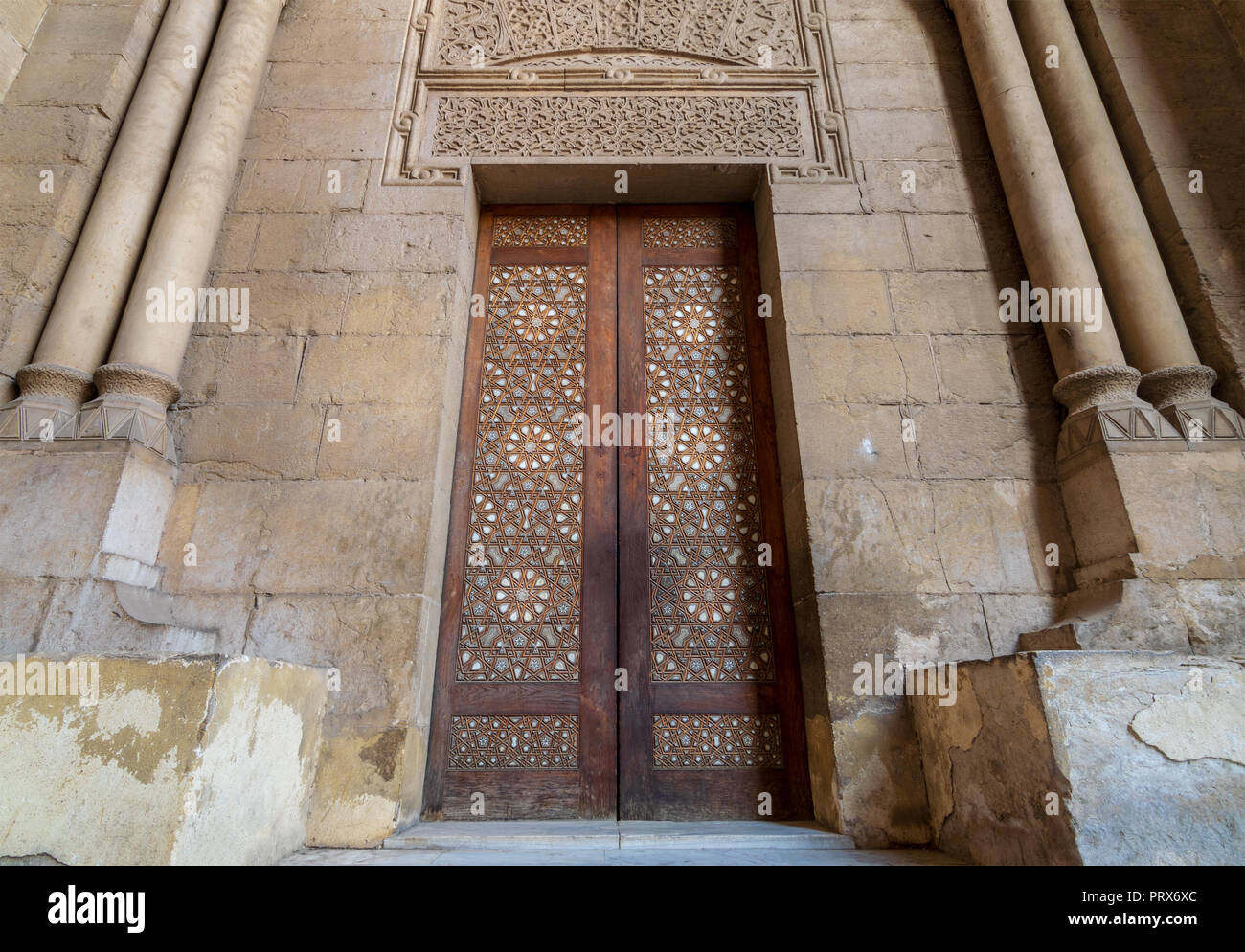 Externe Stil der alten Steine Steinwand mit Arabesque dekoriert Holztür von Stein gerahmt verzierten zylindrische Lichtmasten, die zu Al Rifai Moschee Stockfoto