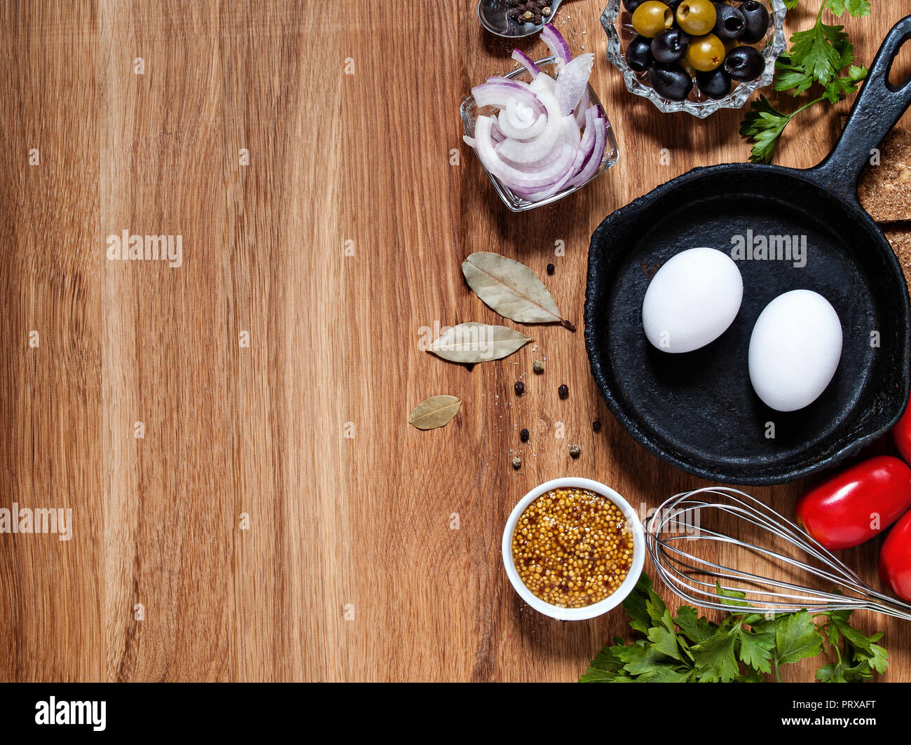 Auf einer hölzernen Hintergrund horizontal mit copyscera huhn eier in einer gusseisernen Pfanne, Zwiebeln, Oliven, Tomaten, grüne, ein Schläger Stockfoto