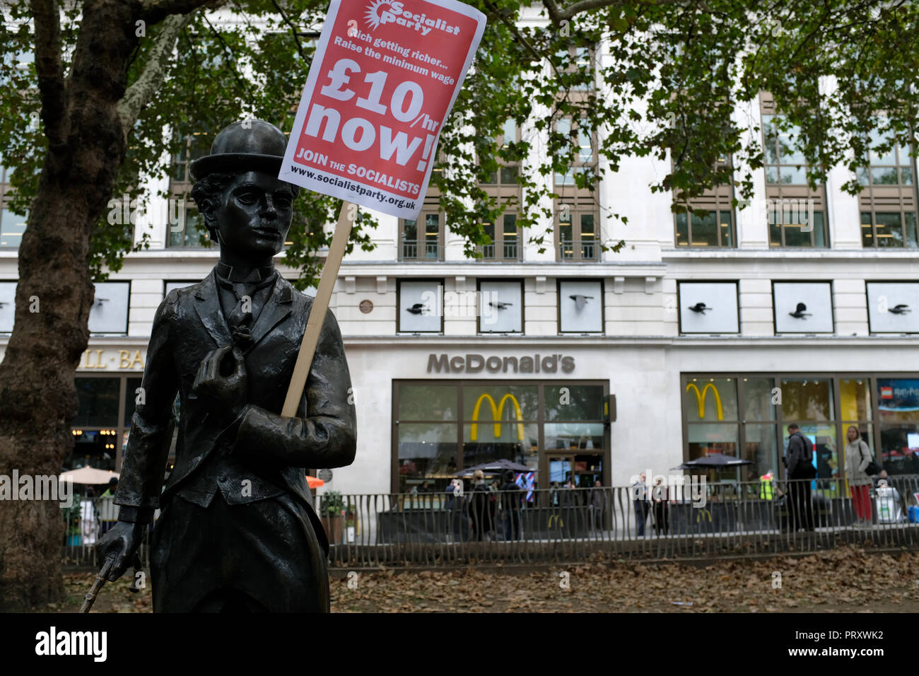 Ein Charles Chaplin Skulptur gesehen mit einem Aushang £ 10/hr Jetzt! Während des Protestes. Wetherspoons, TGI Fridays, und McDonald's Arbeiter Kundgebung zusammen in London, bessere Arbeitsbedingungen und eine angemessene Bezahlung in der Hotellerie zu verlangen. Stockfoto
