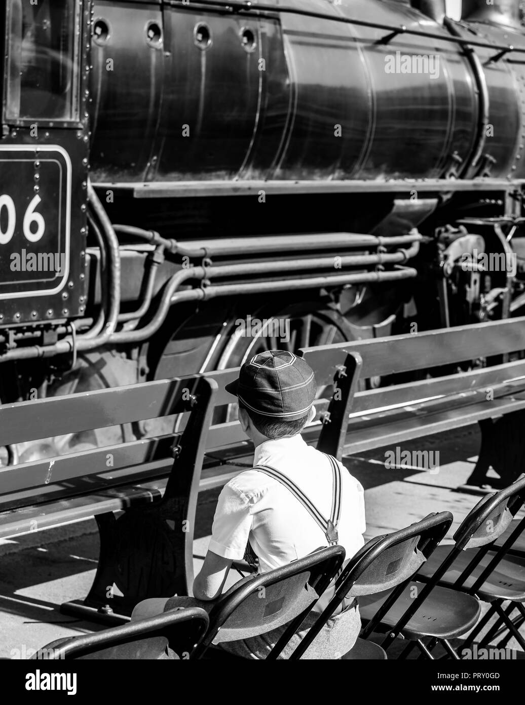 Schwarz & Weiß Rückansicht, Kriegszeiten 1940 Schule Junge in Cap & Hosenträger, sitzen auf Plattform beobachten vintage Dampfzüge träumen, Motor Treiber. Stockfoto