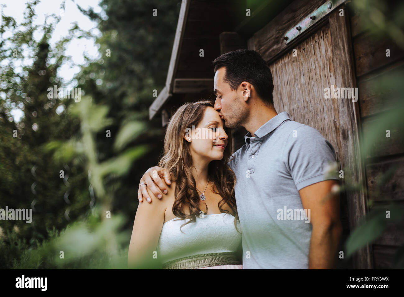 Mann, ist das Küssen seine schwangere Frau auf ihrer Stirn und sie lächelt Stockfoto