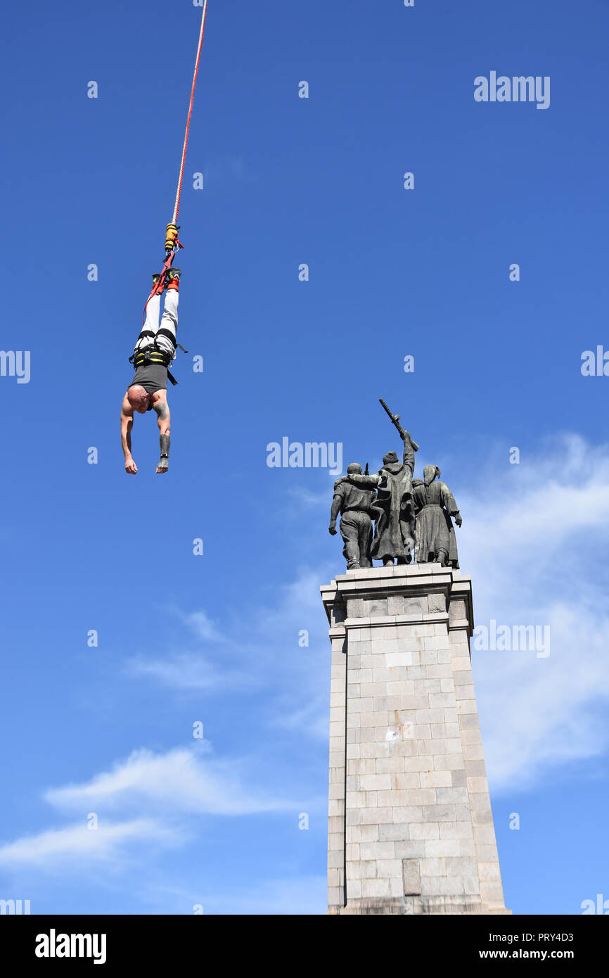 Mann hängen an Kabeljau während Bungeesprung von Kran. Das Denkmal der Sowjetischen Armee in Sofia, Bulgarien - Symbol der Vergangenheit der kommunistischen Zeit hinter ihm gesehen Stockfoto