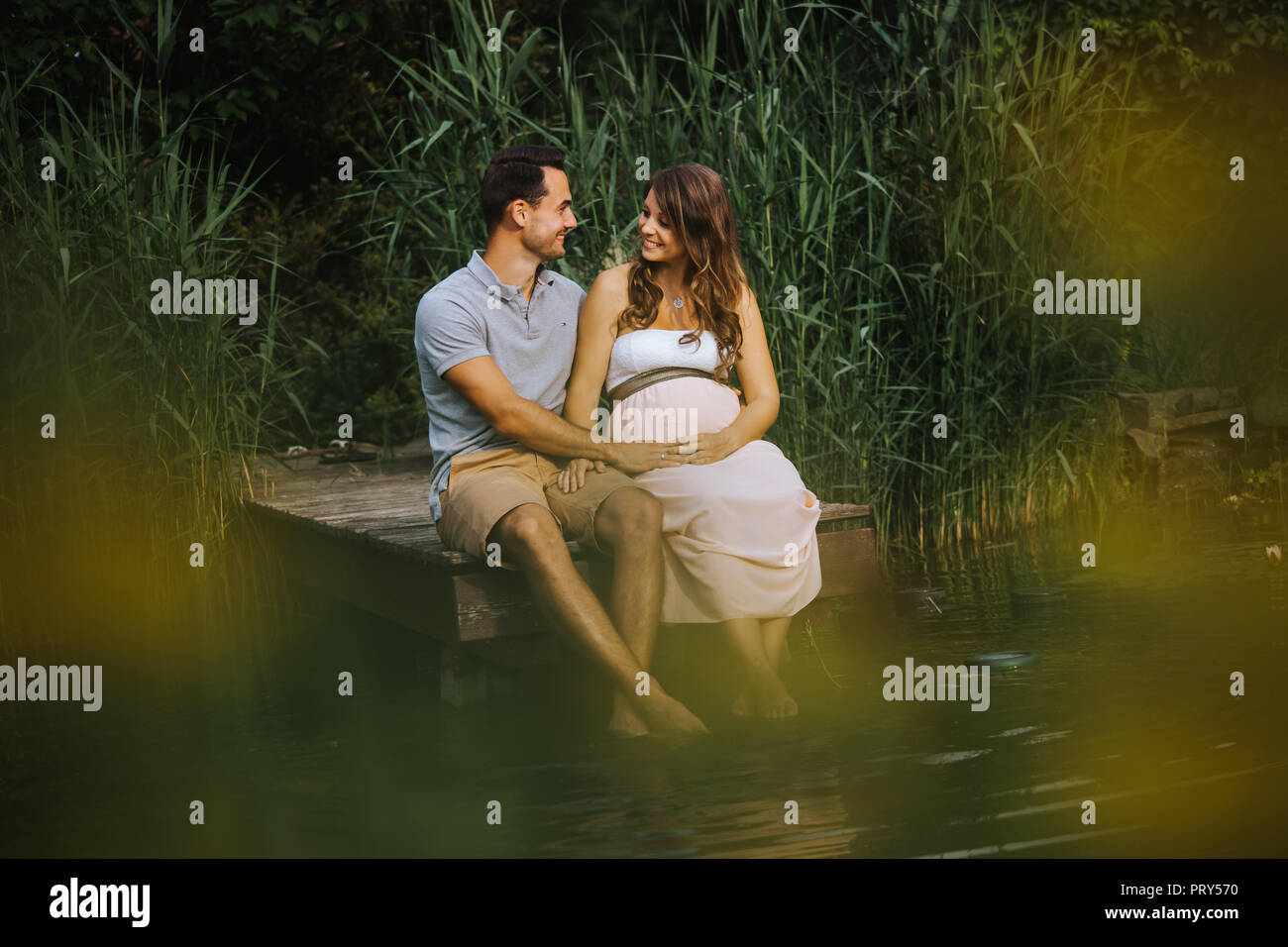 Schwangere Frau und ihr Mann sitzen an einem See und die gemeinsame Zeit genießen. Stockfoto