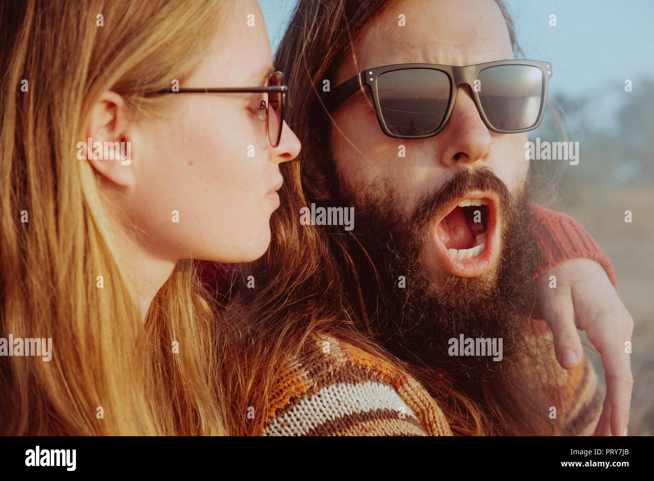 Lächelnd hipster Paar in Sonnenbrille umarmen und Spaß im Freien in Sunrise. Mann und die blonde Frau mit Bart. Stockfoto