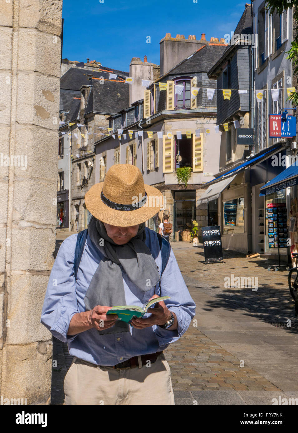REISEFÜHRER ERKUNDEN SIE DIE FRANZÖSISCHE Altstadt mit einem männlichen Touristen, der einen Sonnenhut trägt und einen Michelin Brittany Tourist Guide Quimper Brittany liest Stockfoto