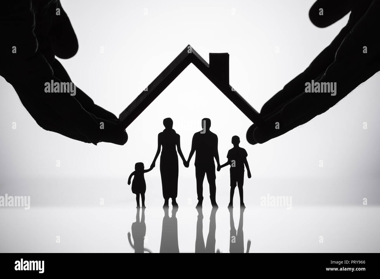 Ist eine Person, die schützende Hand Familie Figuren mit Dach auf reflektierende Schreibtisch Stockfoto
