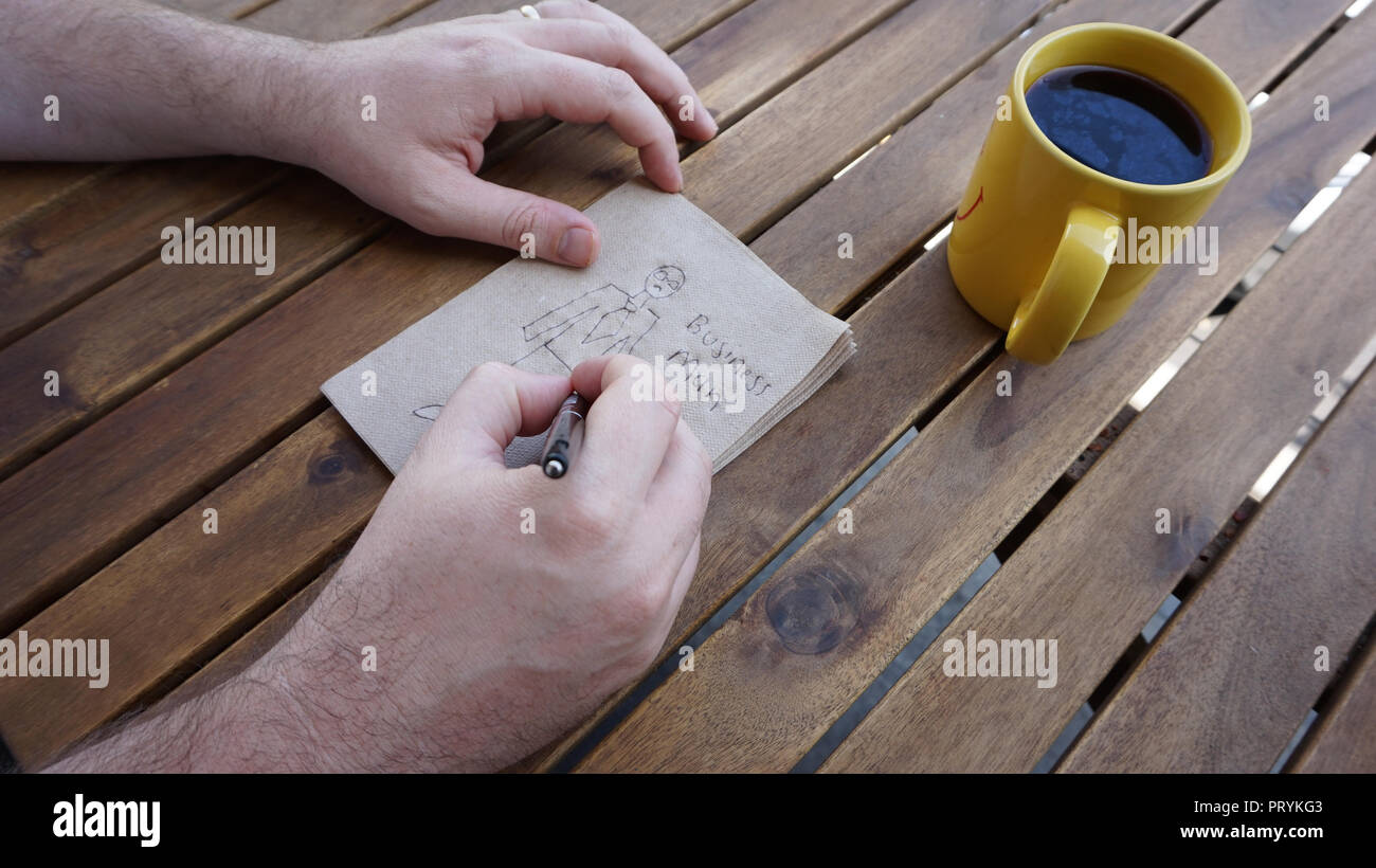'Business'-nachdenklichen Mann Skizzen ein Mann in Anzug und Krawatte auf eine Serviette, während er trinkt eine Tasse Kaffee. Stockfoto