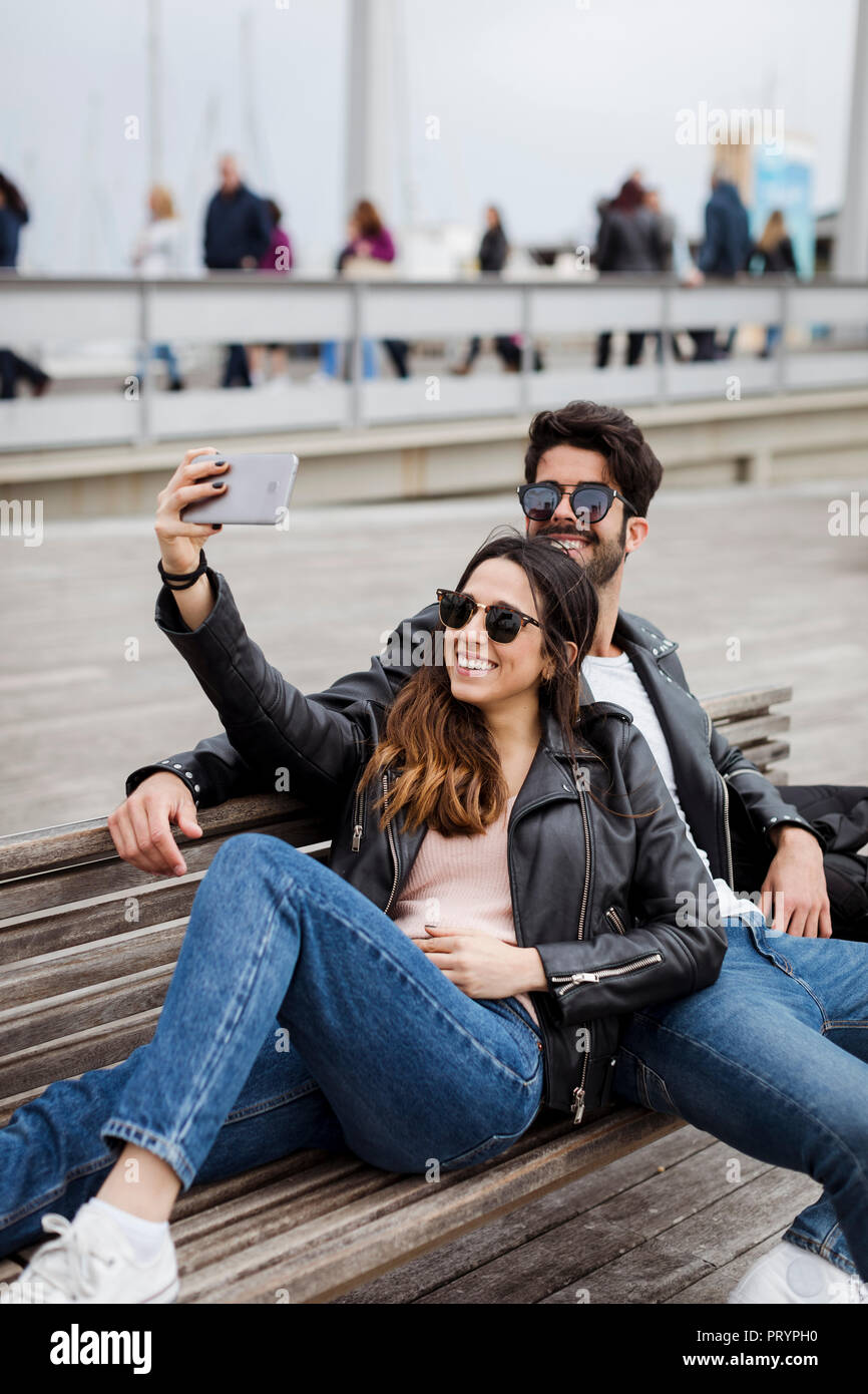 Spanien, Barcelona, glückliches junges Paar auf einer Bank unter einem selfie Stockfoto