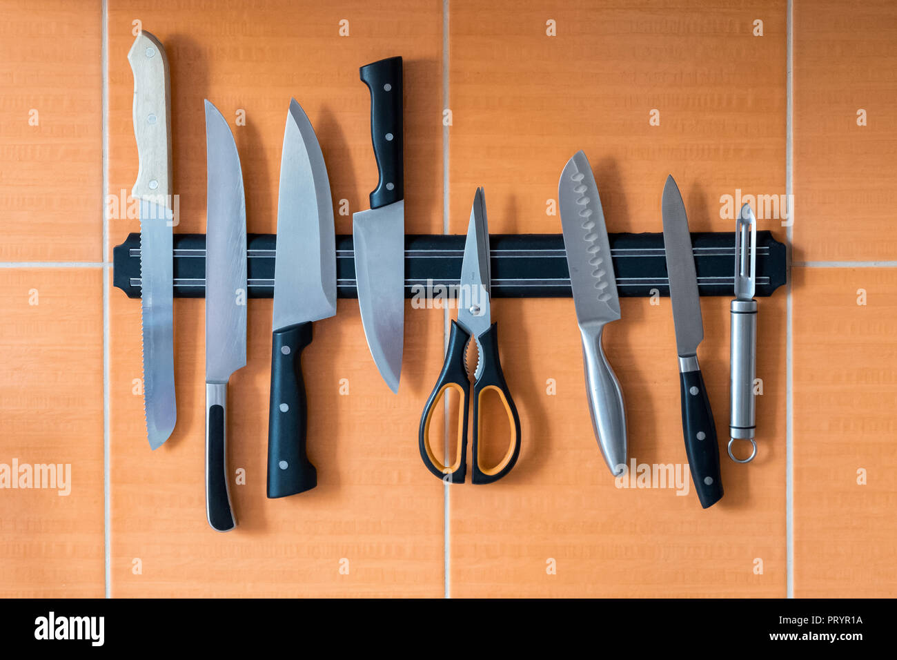 Die Messer hängen an einem Magnethalter. Orangefarbene Küchenwand. Eine Methode zur Aufbewahrung scharfer Gegenstände in der Küche Stockfoto