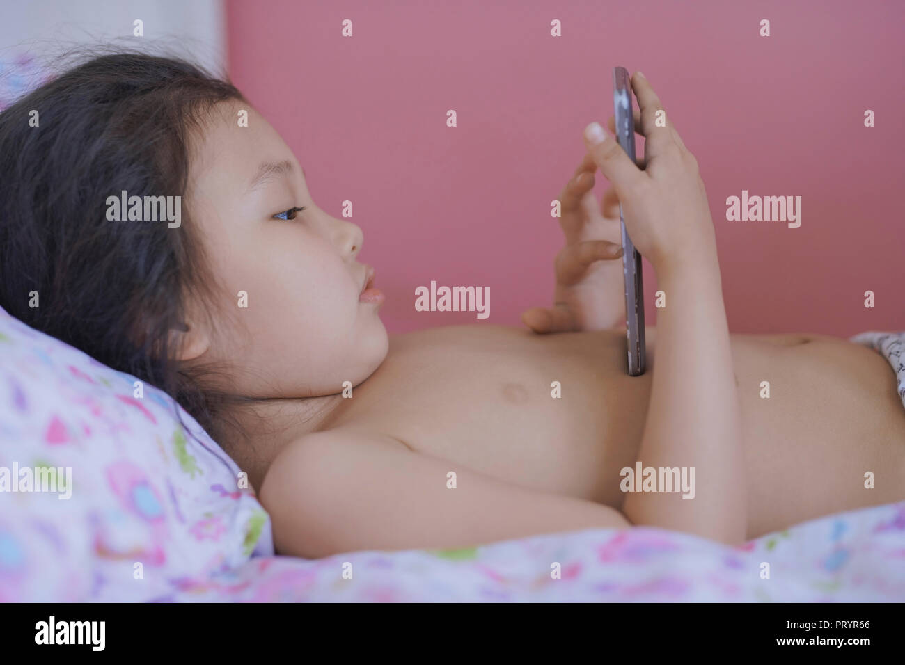 Kleines Mädchen auf dem Bett liegend Spielen mit Smartphone Stockfoto