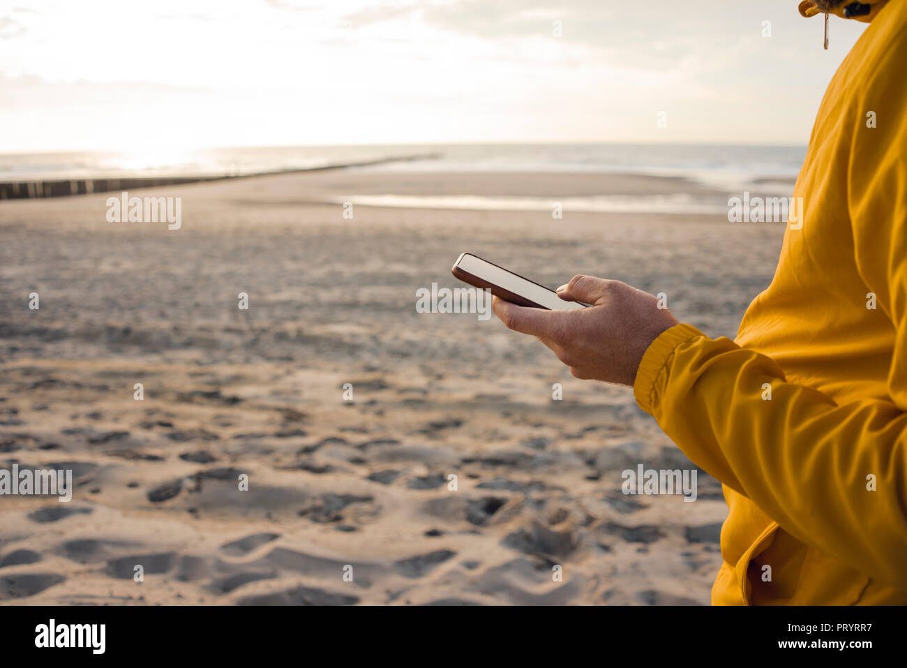 Mann in der gelben Jacke, Sie ihr Smartphone am Strand Stockfoto