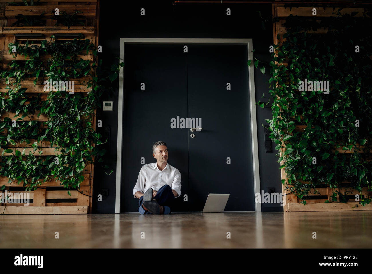 Geschäftsmann mit Laptop sitzen auf dem Boden im grünen Büro Stockfoto