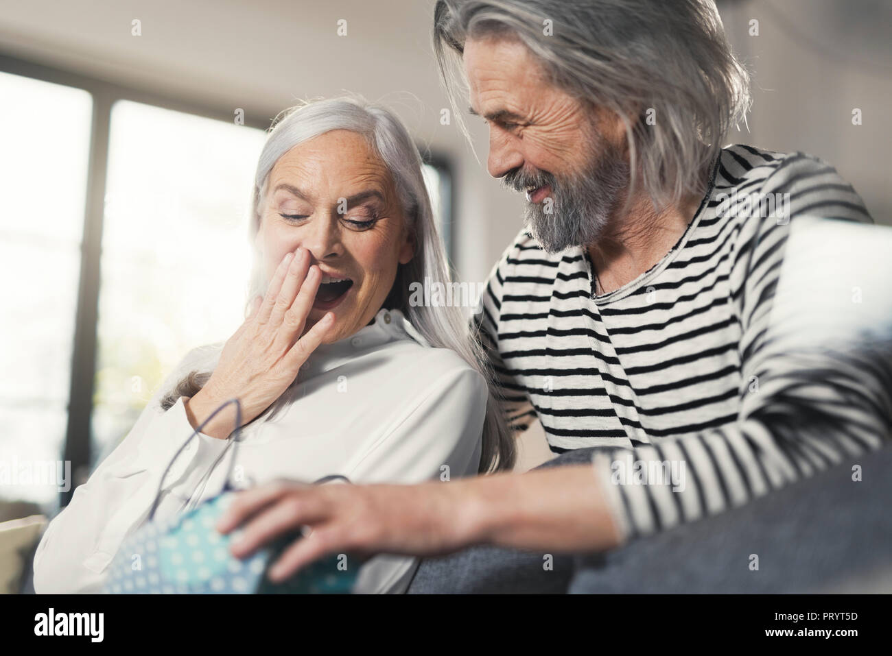 Älterer Mann überraschend Frau mit einem Geschenk Stockfoto