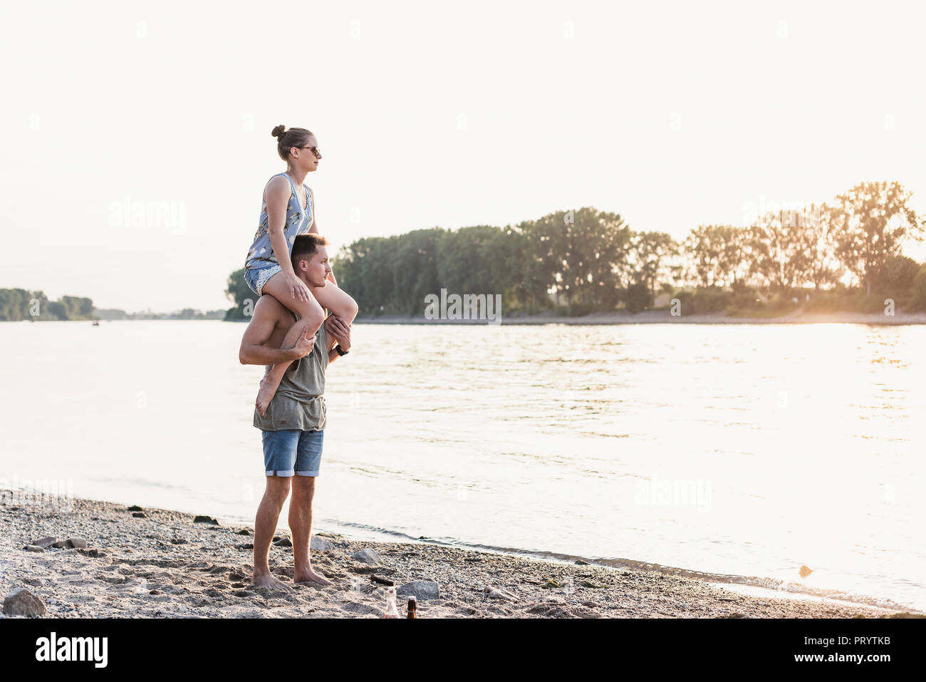 Junger Mann mit Freundin auf den Schultern am Flussufer Stockfoto