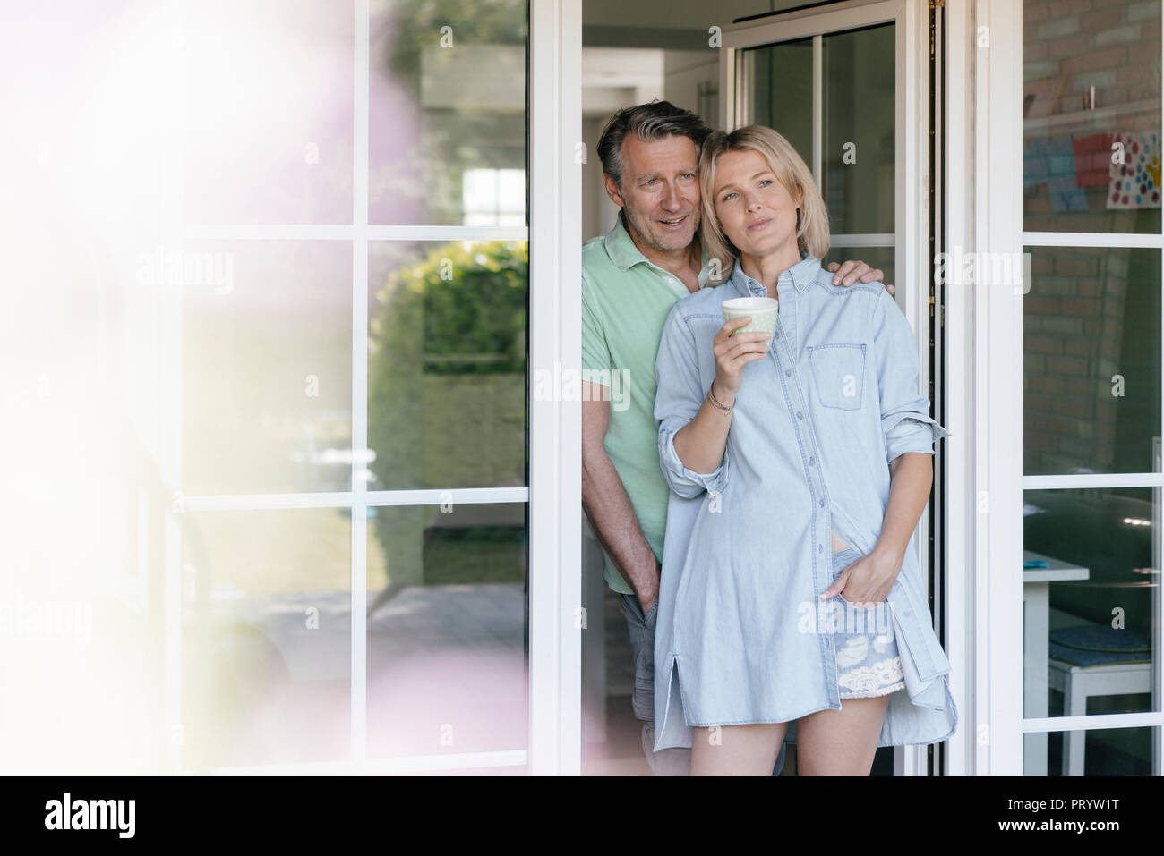 Lächelnd reifes Paar stehend an französische Fenster Stockfoto