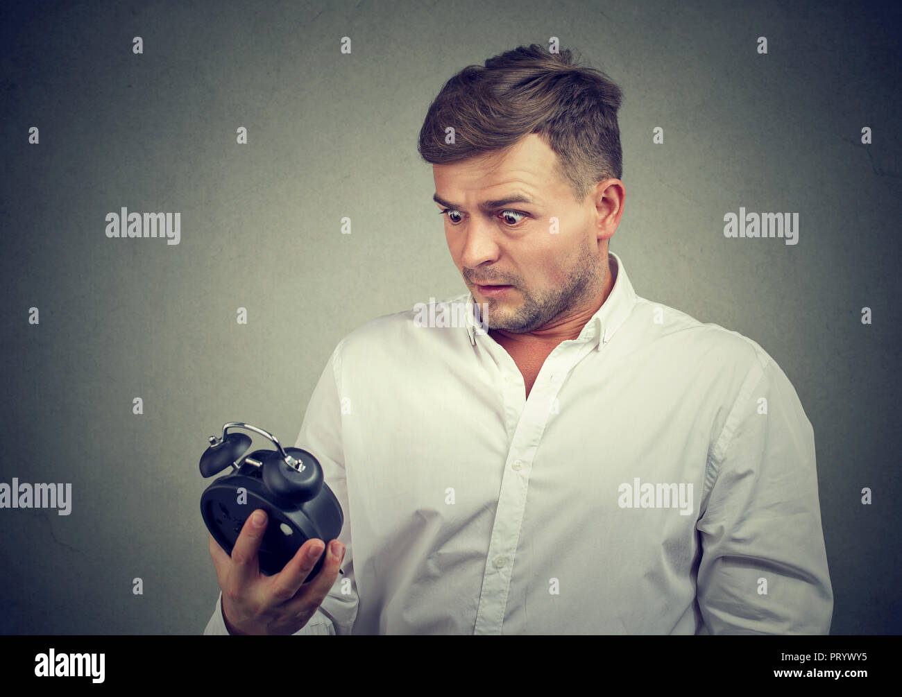 Junger Mann in formalen shirt Wecker suchen mit Angst spät auf grauem Hintergrund, Stockfoto