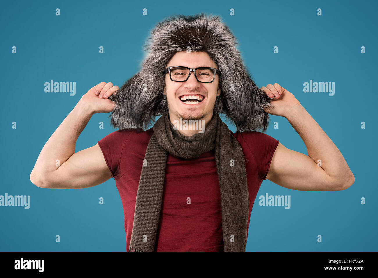 Junger Mann mit trendigen Furry winter Mütze und Schal glücklich Kamera schaut auf grauem Hintergrund Stockfoto