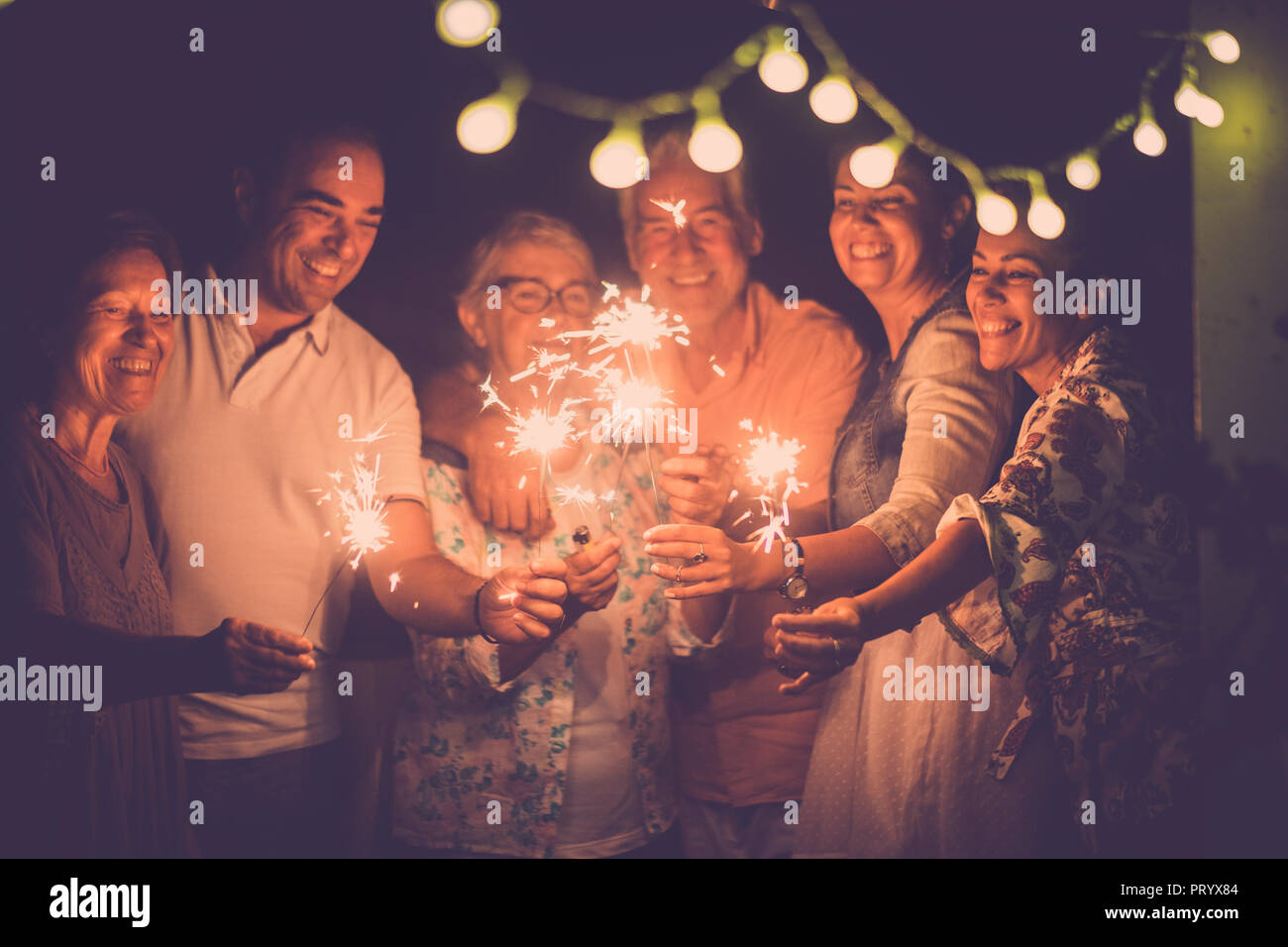 Gruppe der kaukasischen Völker Freunde mit unterschiedlichen Alters feiern zusammen einen Geburtstag oder Silvester in der Nacht zu Hause outdoor. leuchtet und funkelt wit Stockfoto