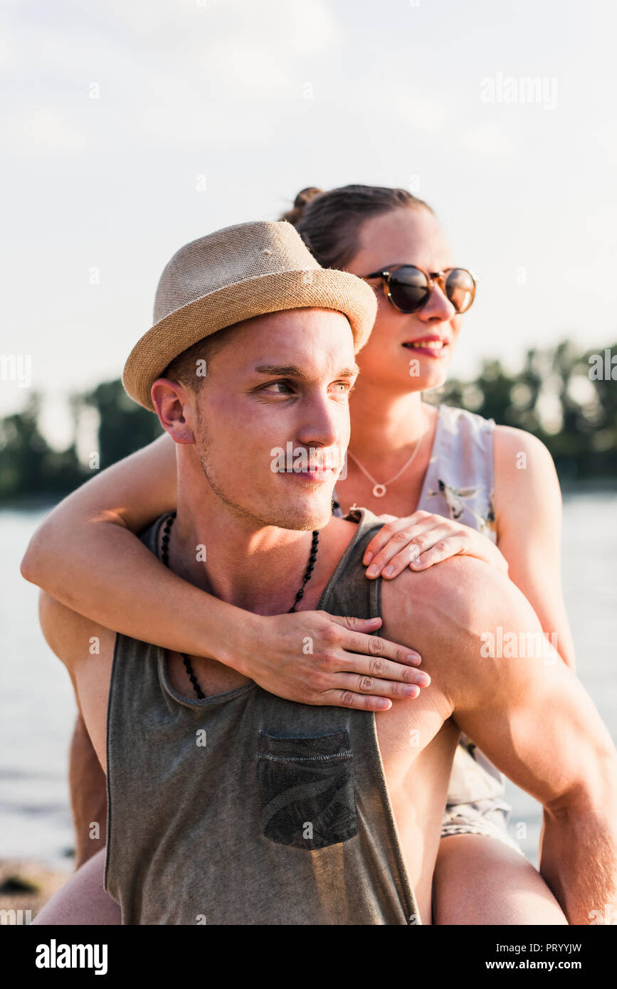 Junger Mann, Freundin piggyback Ride am Flussufer Stockfoto