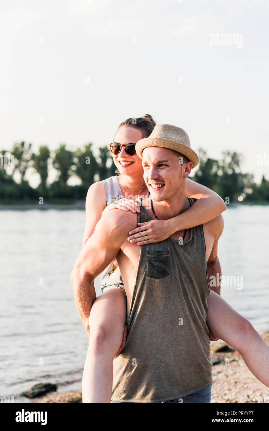 Junger Mann, Freundin piggyback Ride am Flussufer Stockfoto
