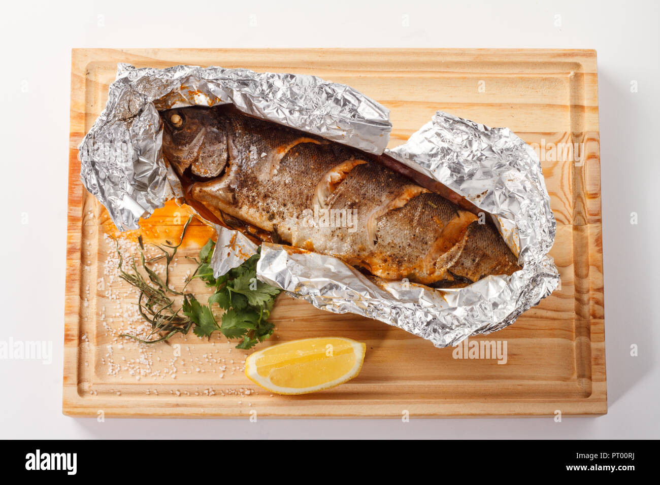 Gerösteter Forellenfisch mit Kräutern und Zitrone auf einem Holzbrett. Stockfoto