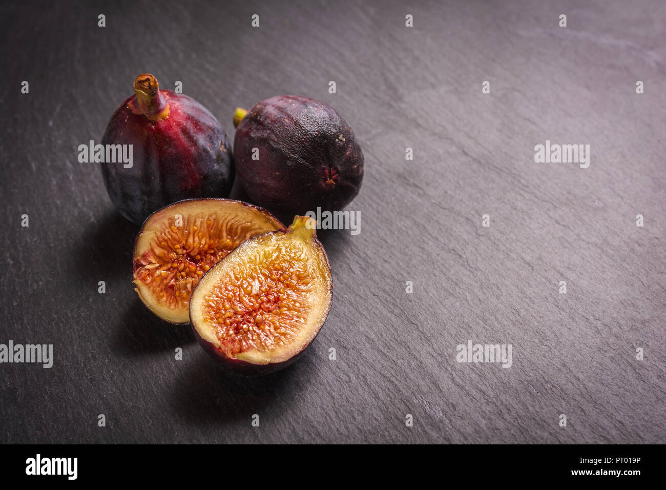 Gruppierung von Feigen, einem Schnitt mit offenem Blattgewebe der Frucht auf Schiefer zu zeigen. Stockfoto