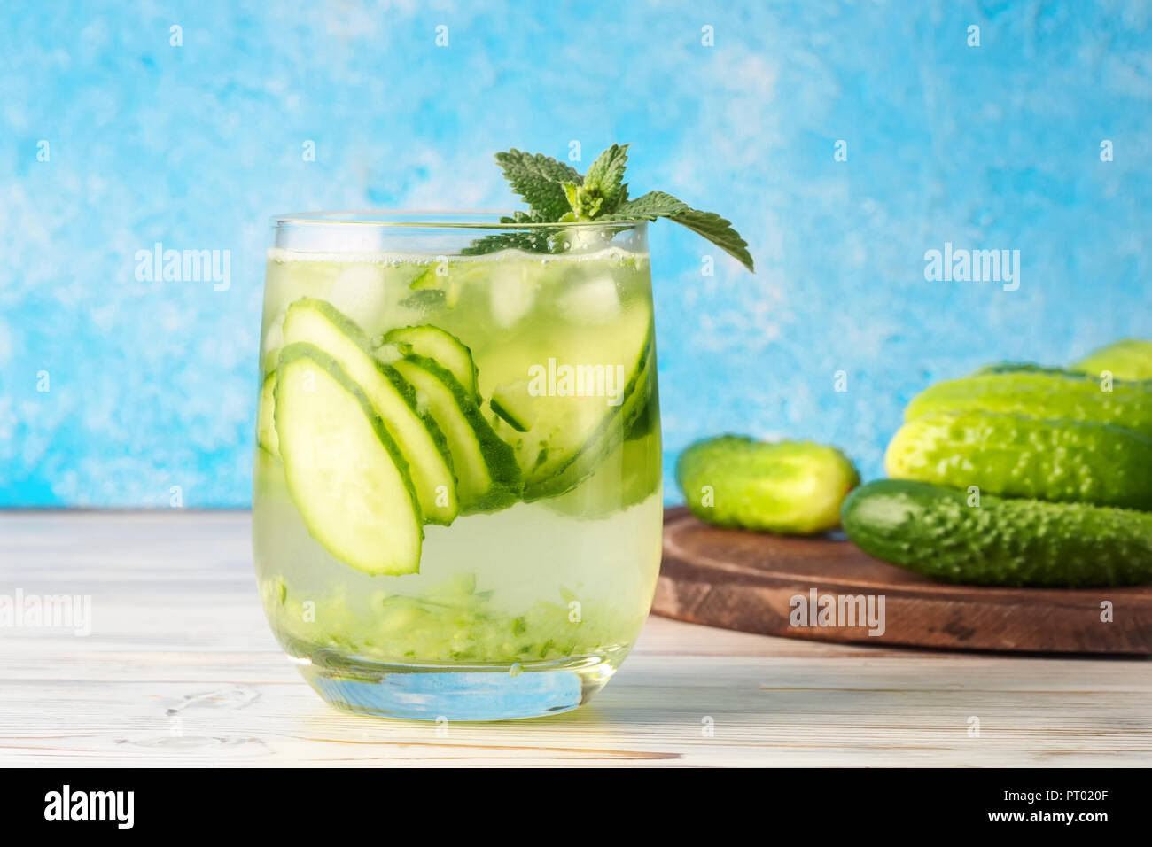 Gurken Wasser mit Minze ist beliebt detox drink Glas von antioxidativen Infusion mit Scheiben von Gemüse am Küchentisch und blauer Hintergrund Stockfoto
