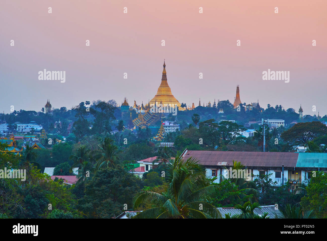 Die grüne Singuttara Hügel mit hoch aufragenden Shwedagon Pagode und Silhouetten von kleineren Stupas in dim Twilight, Yangon, Myanmar. Stockfoto