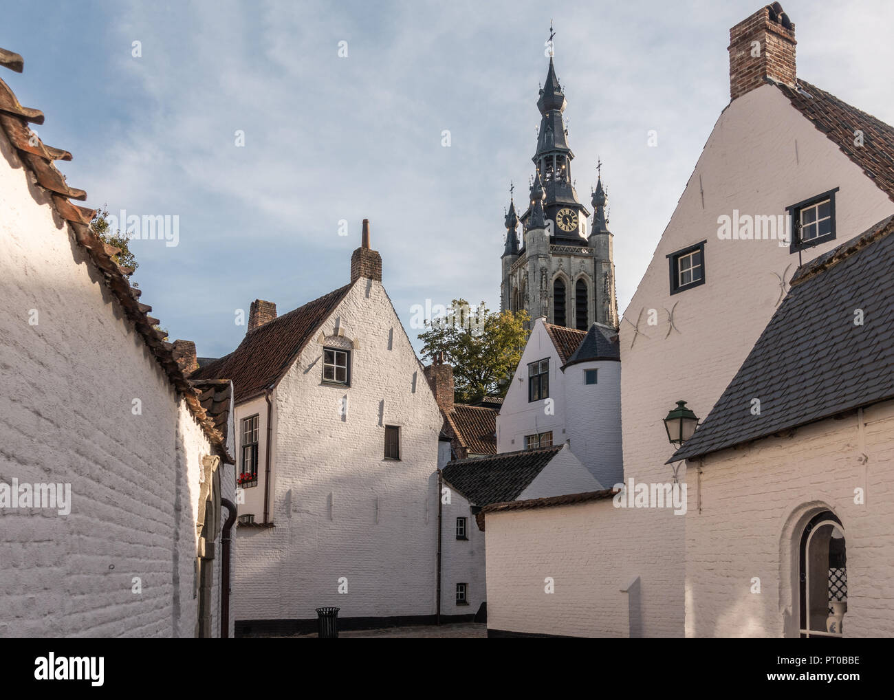 Kortrijk, Flandern, Belgien - 17. September 2018: Turm der Kirche Notre Dame von Ecke gesehen der Beginenhof mit weißen und roten überdachte Gehäuse. Einige gre Stockfoto