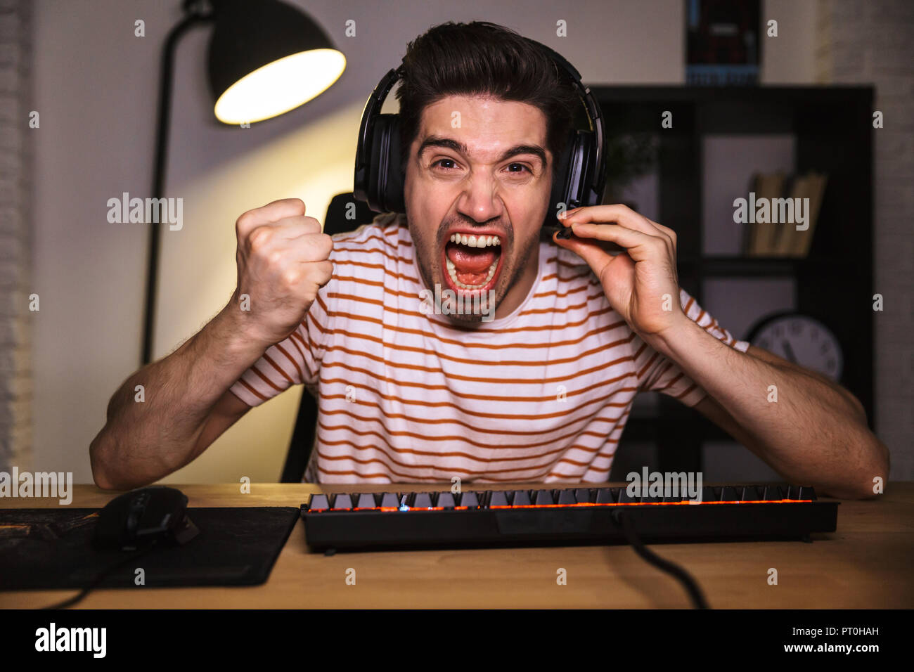 Schreien angry gamer Videospiele auf Computer, während durch die Tabelle zu Hause sitzen Stockfoto