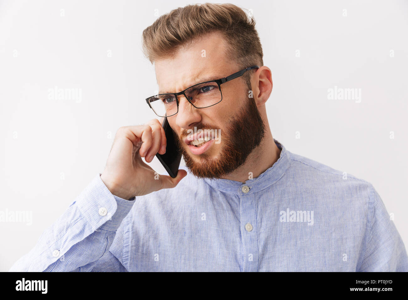 Portrait eines wütenden jungen bärtigen Mann in Brillen über Weiß isoliert stehen, Gespräch am Handy Stockfoto