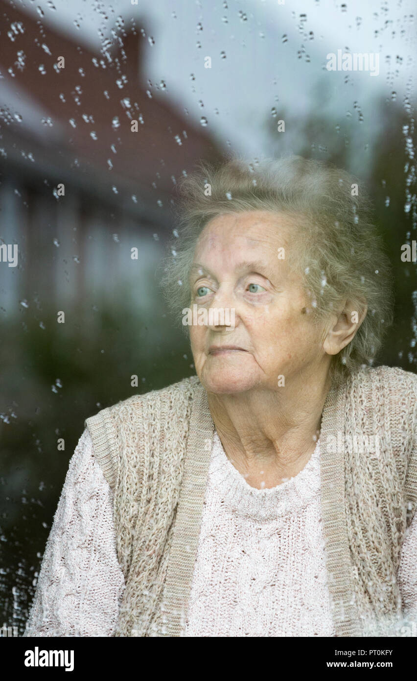 Neunzigjährige Frau, die an einem regnerischen Tag aus dem Fenster schaut. Selbstisolation, Quarantäne, Coronavirus, Konzept der sozialen Distanzierung... Stockfoto