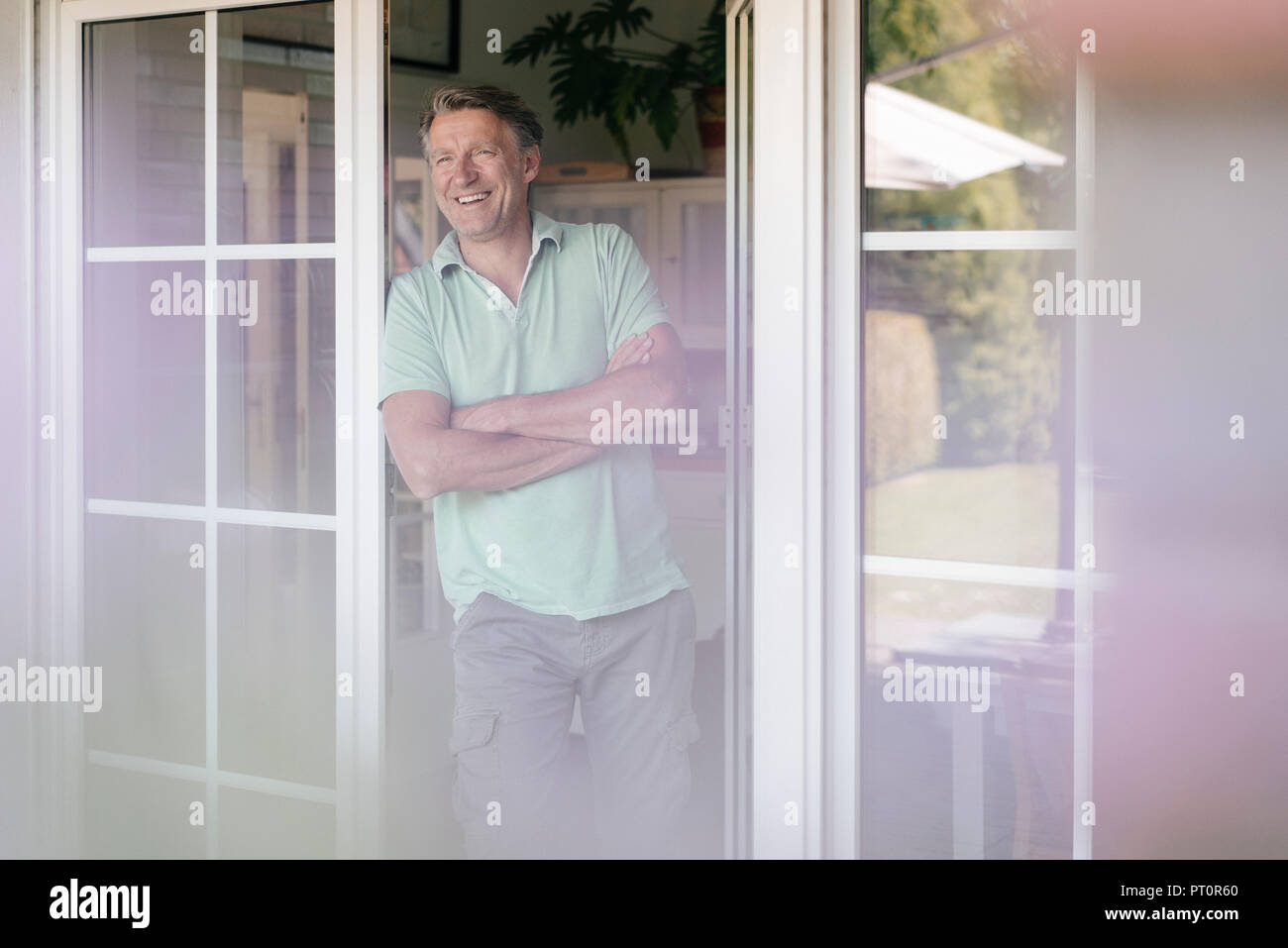 Lachend reifer Mann stehend an französische Fenster Stockfoto