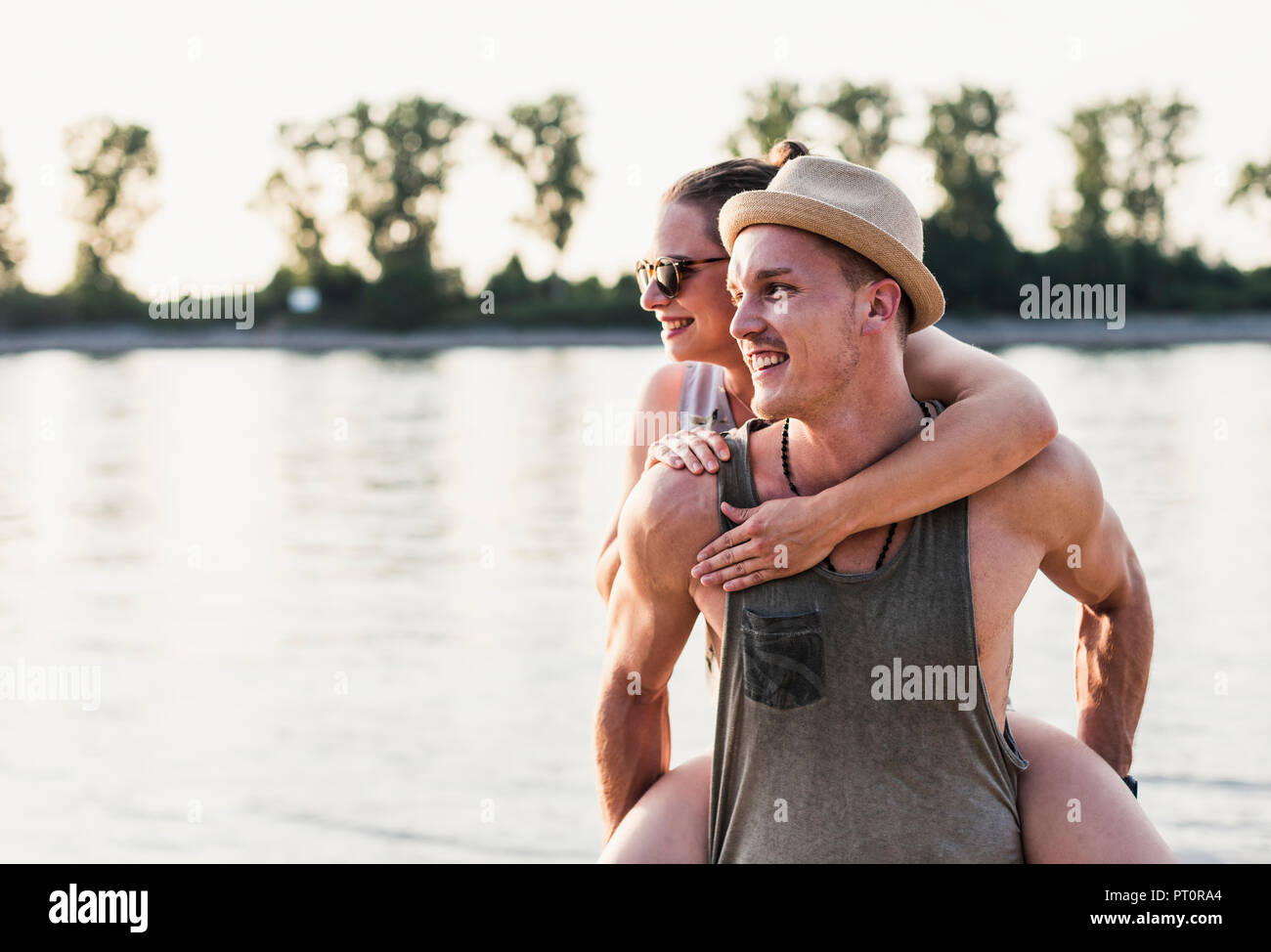 Junger Mann, Freundin piggyback Ride am Flussufer Stockfoto