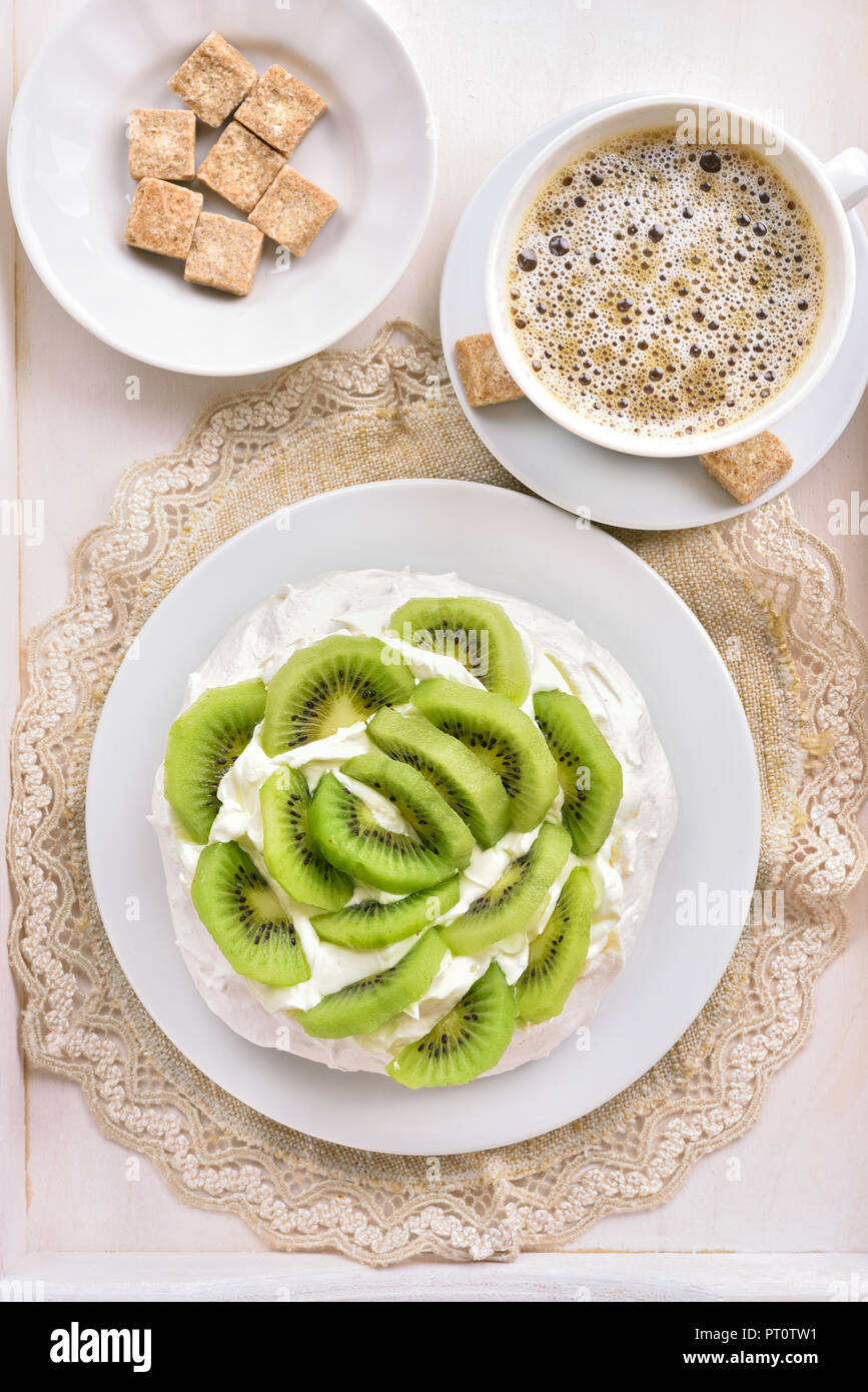 Lecker pavlova Baiser Kuchen mit Kiwi Scheiben anf Tasse Kaffee. Ansicht von oben, flach Stockfoto