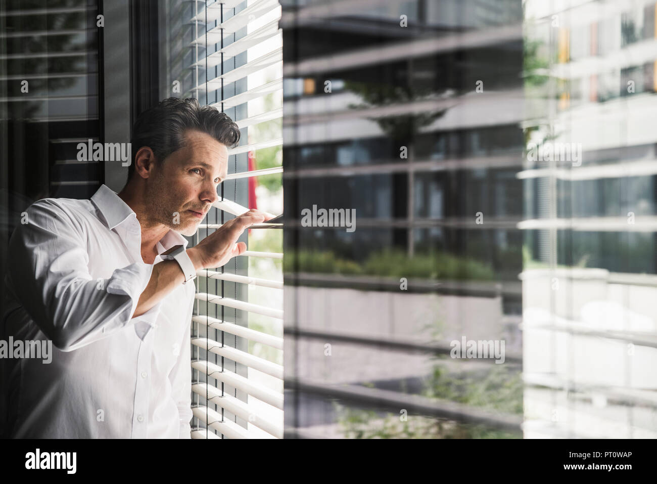 Geschäftsmann spähen durch Markisen am Fenster im Büro Stockfoto