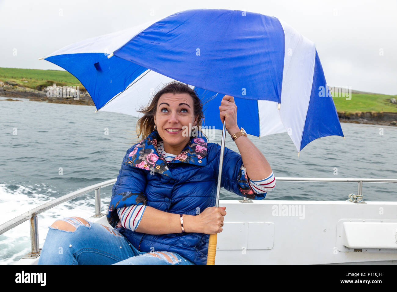 Blonde Frau auf einem Boot mit kaputten Regenschirm Stockfoto