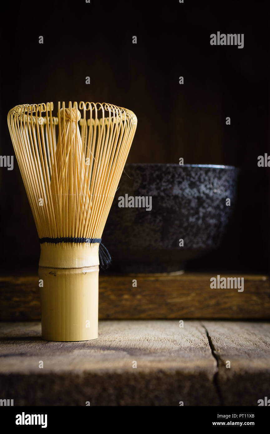 Japanische Matcha Grüntee Schneebesen oder Chasen mit einem Defokussierten chawan oder traditionelle Keramik Schüssel im Hintergrund mit dunklen stimmungsvolle Beleuchtung Stockfoto