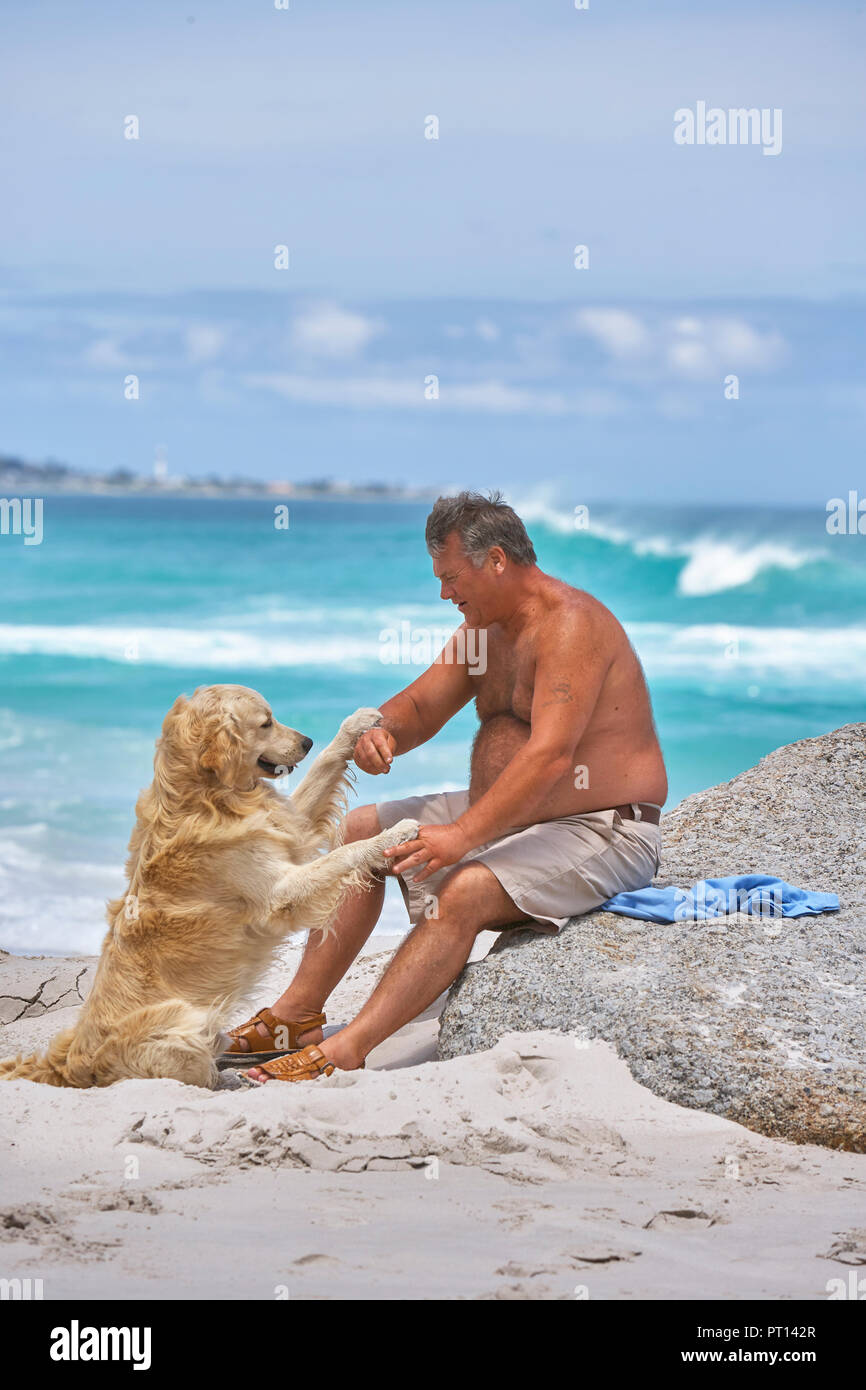 Fetter Mann mit seinem Hund am Strand Stockfoto