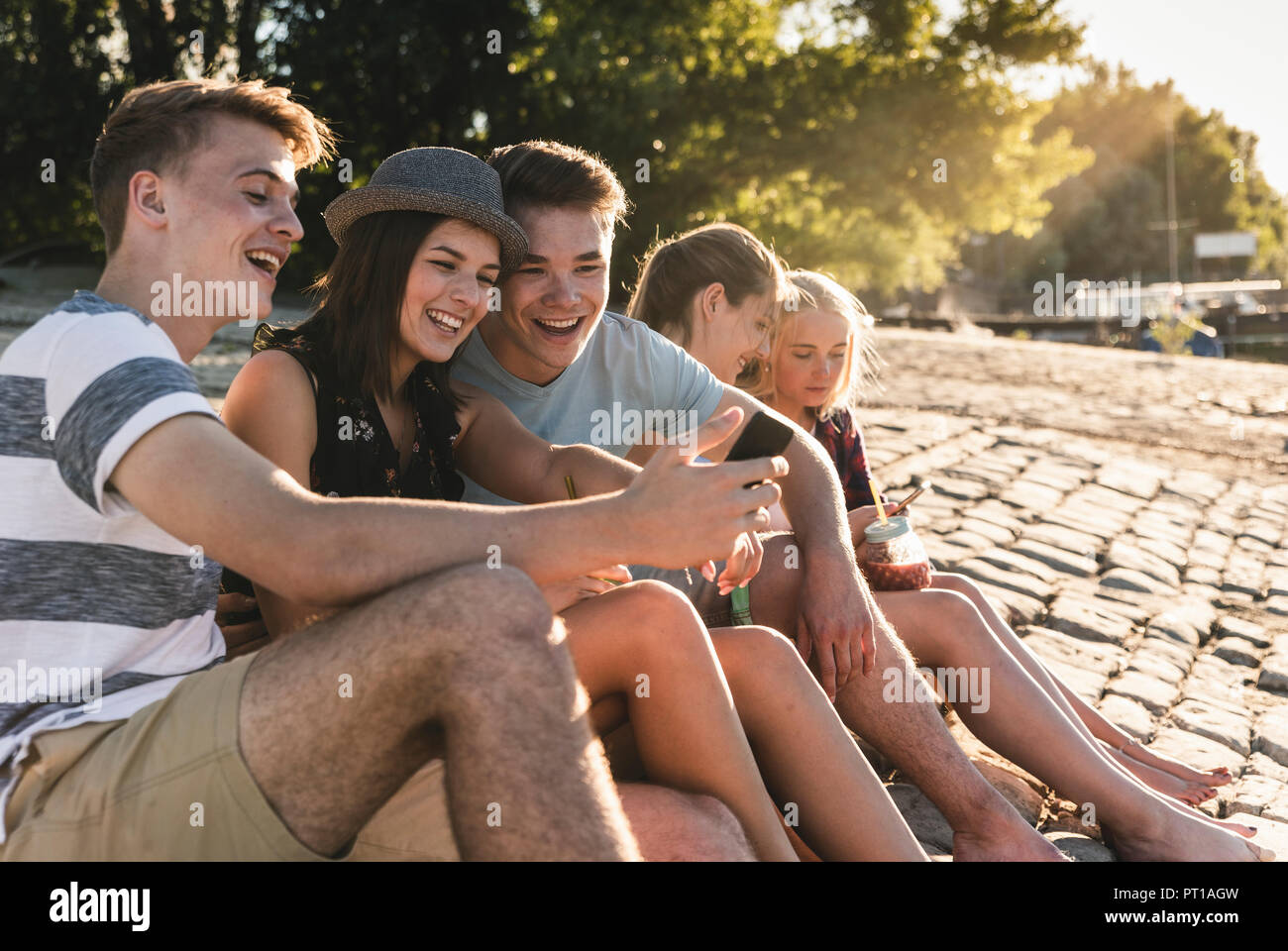 Gruppe von Freunden sitzen auf Kopfsteinpflaster mit erfrischenden Getränken und Mobiltelefone Stockfoto