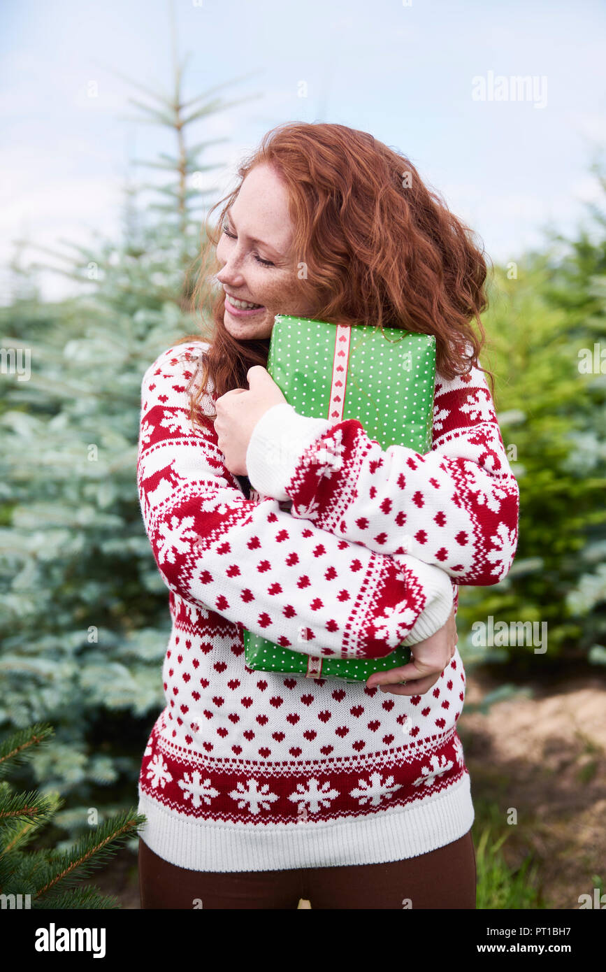 Happy rothaarige Junge Frau umarmt Weihnachtsgeschenk im Freien Stockfoto