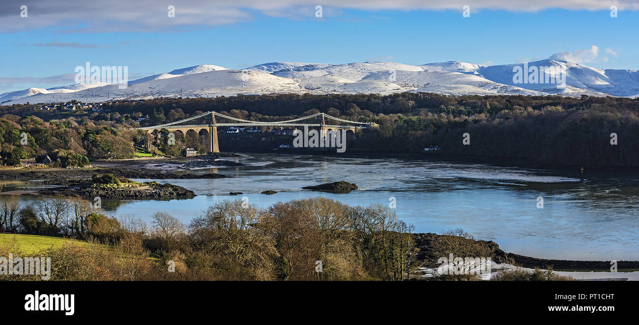 Menai Suspension Bridge, entworfen von Thomas Telford gesehen von Anglesey über die Menai Strait mit schneebedeckten Hügeln im Hintergrund North Wales Stockfoto