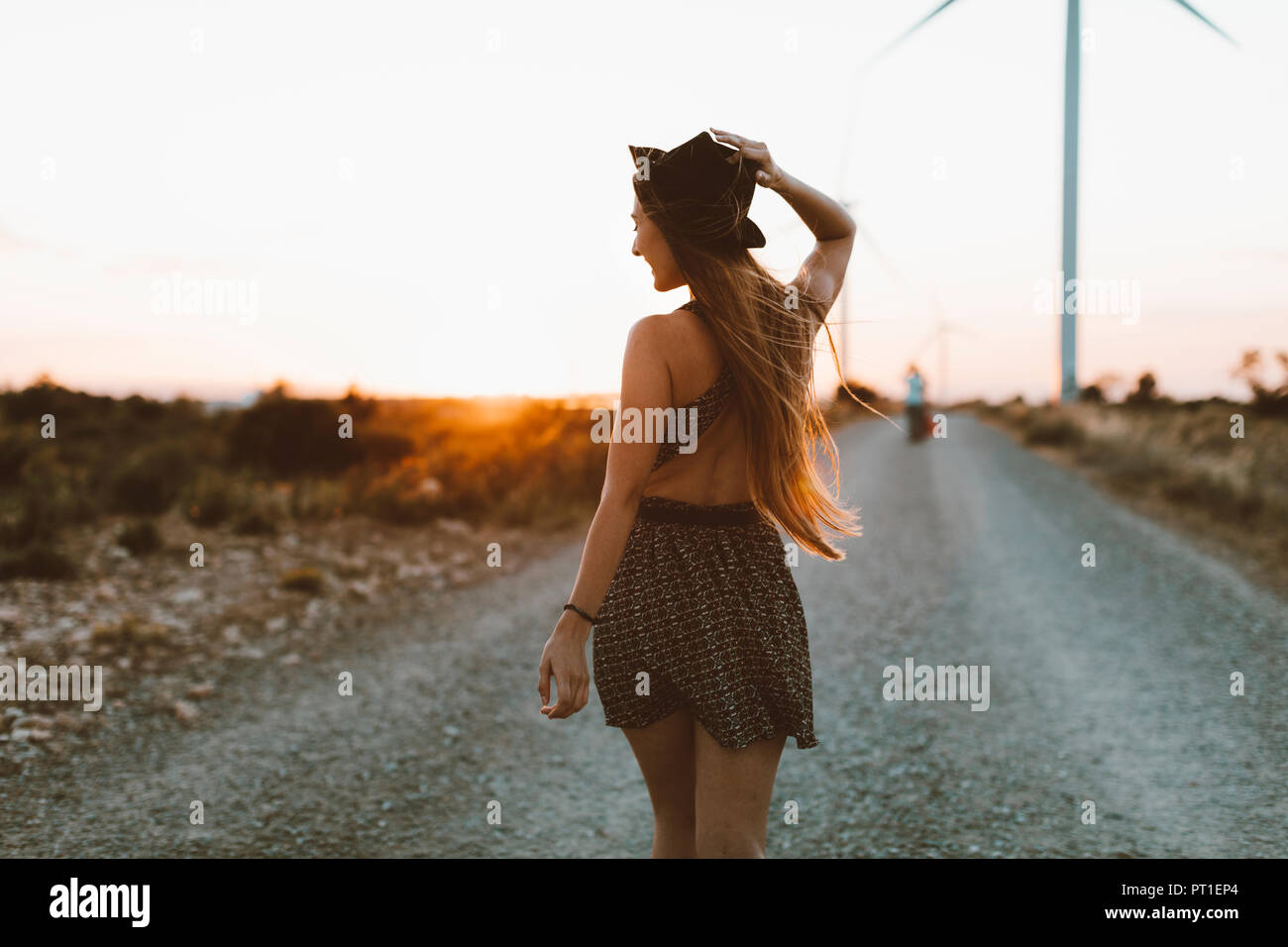 Zurück Blick auf die junge Frau zu Fuß auf die ländliche Straße am Abend dämmerung Stockfoto