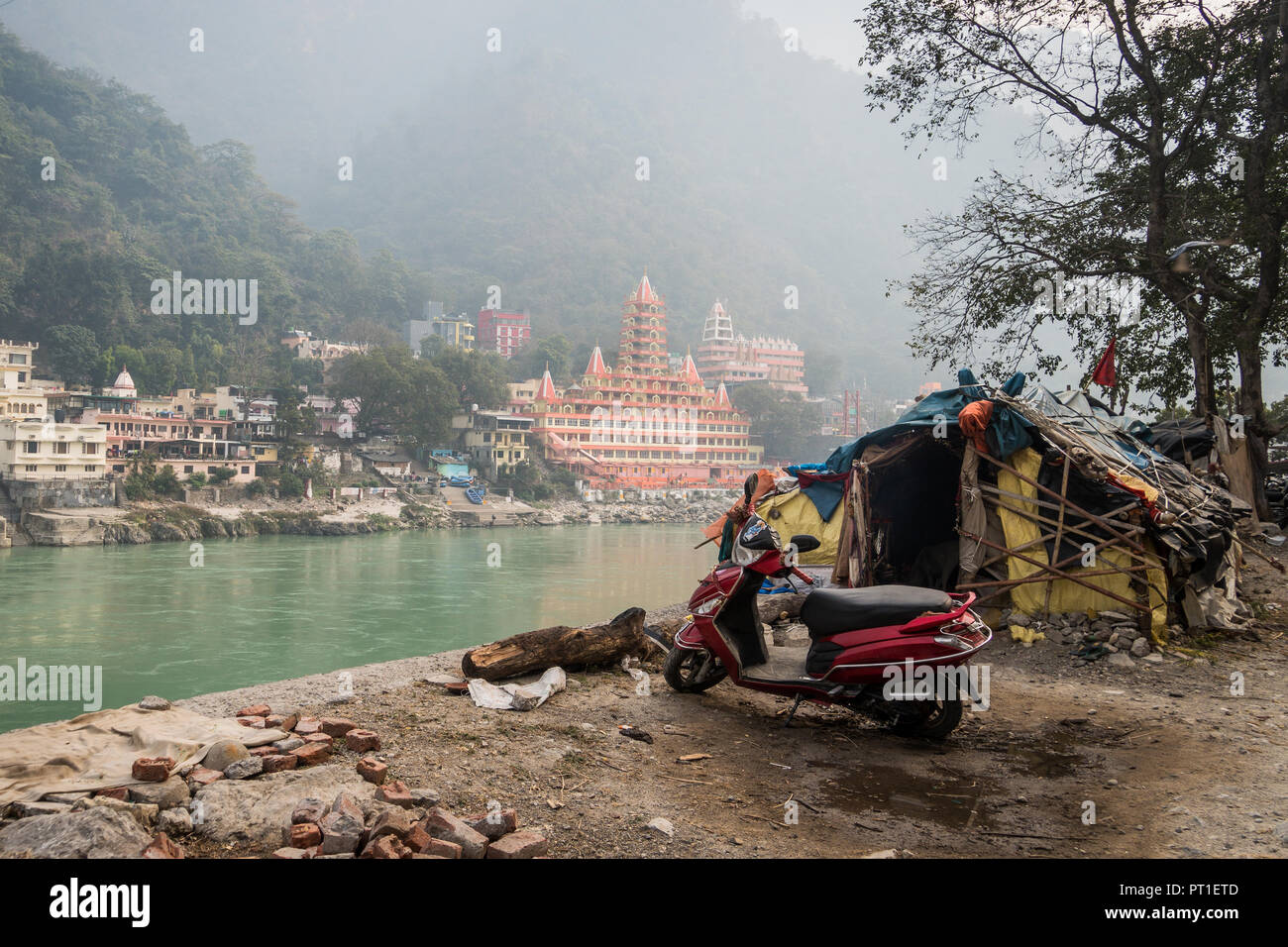 Beggar's Hütte am Fluss Ganges, Rishikesh auf dem Hintergrund einer umfangreichen teuren Tempel auf der anderen Seite des Flusses. Die soziale Ungleichheit. Den üblichen Fehlermeldungsprozeduren Stockfoto
